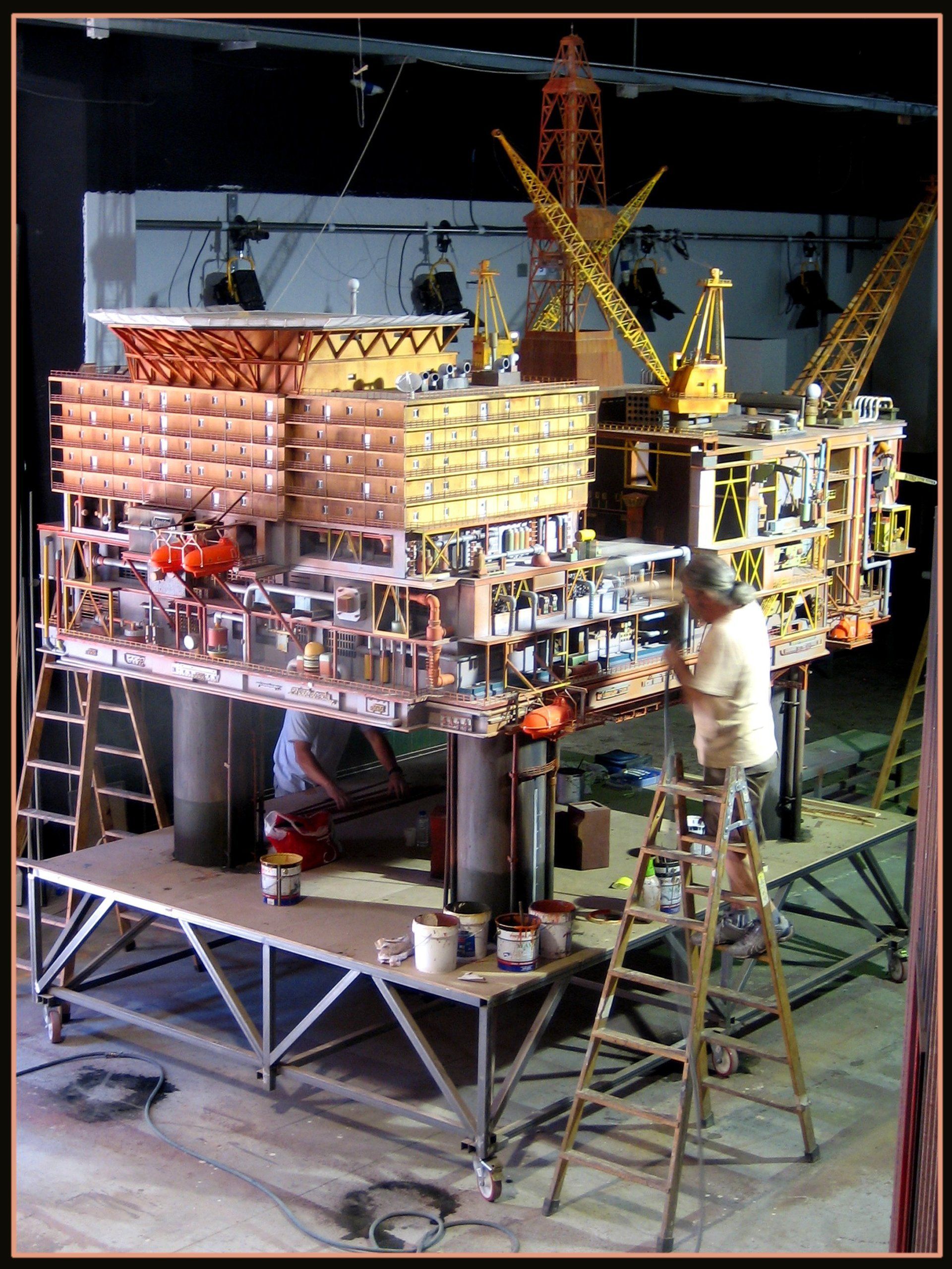 Un hombre en una escalera trabajando en un modelo de una plataforma petrolera.