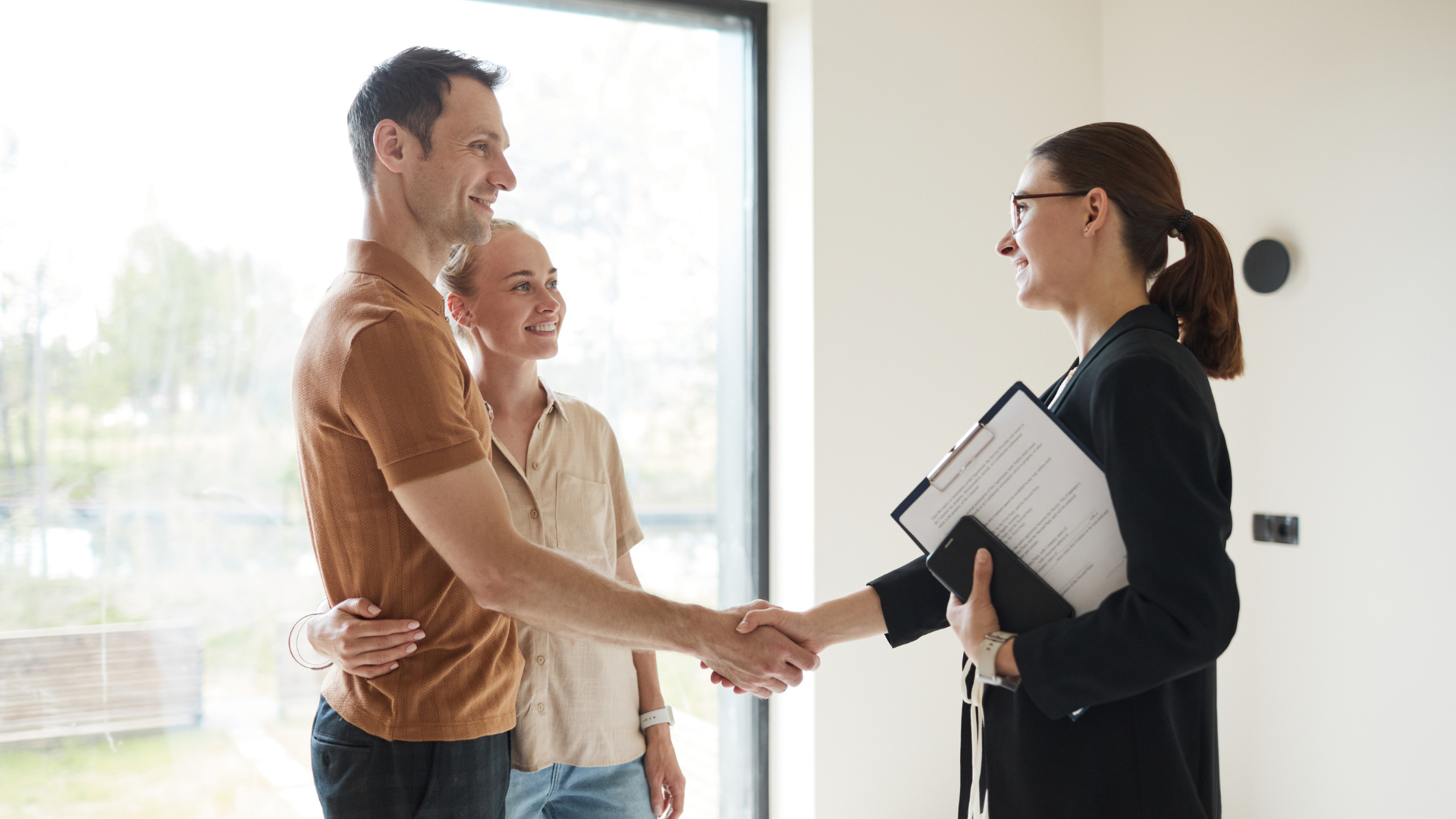 A man and woman are shaking hands with a real estate agent.