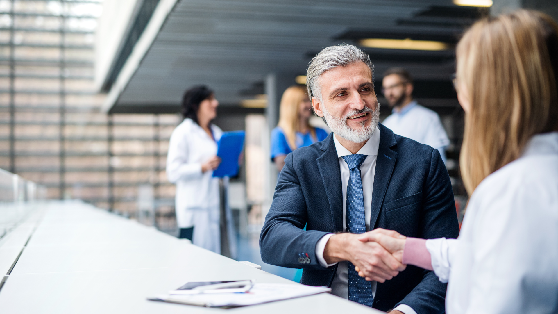 A man in a suit and tie is shaking hands with a woman in a lab coat.