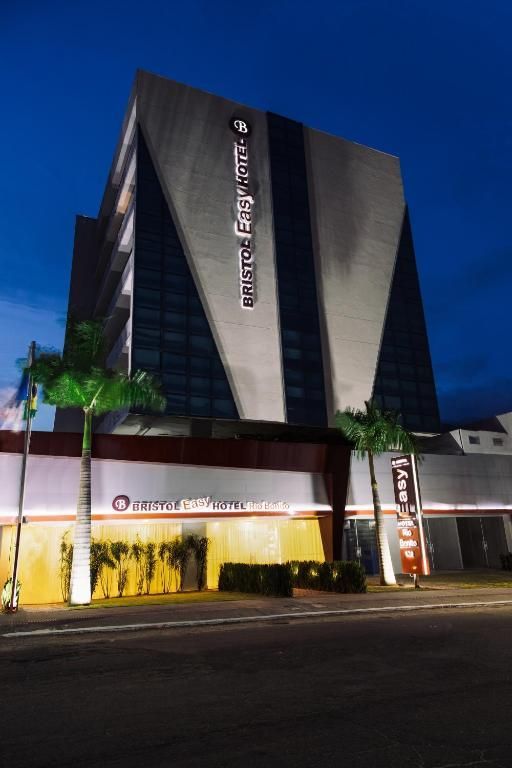 Edifício de hotel ao entardecer, com fachada inclinada, palmeiras e uma placa iluminada.