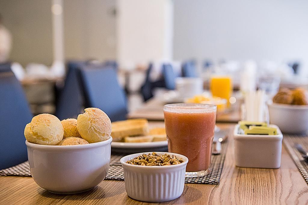 Mesa de café da manhã: pãezinhos, suco, torrada, kiwi e sementes.