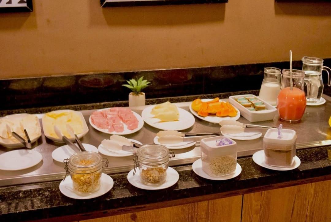 Buffet de café da manhã com queijos, frios, doces, iogurte, sucos e leite.