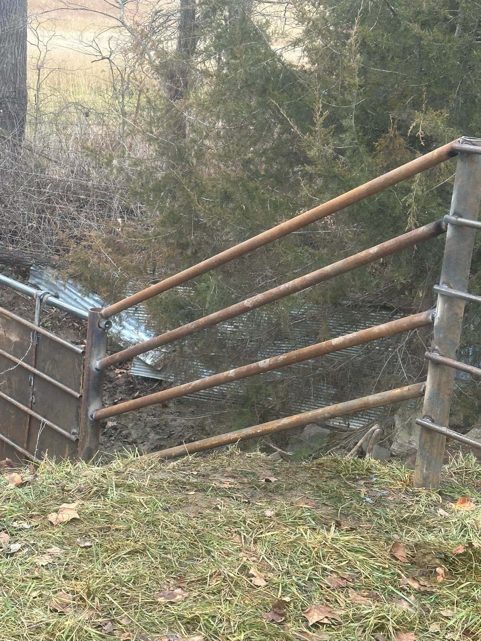 A wooden fence with a metal railing is surrounded by grass and trees.