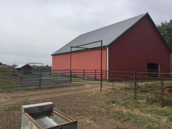 A red barn with a fence around it and a water trough in front of it.