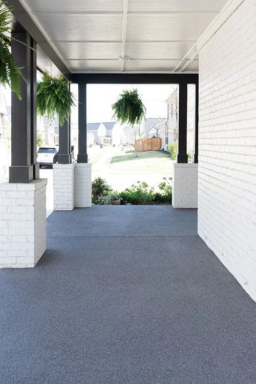 Modern white house entrance with gray trim, front porch, flowers, and green lawn