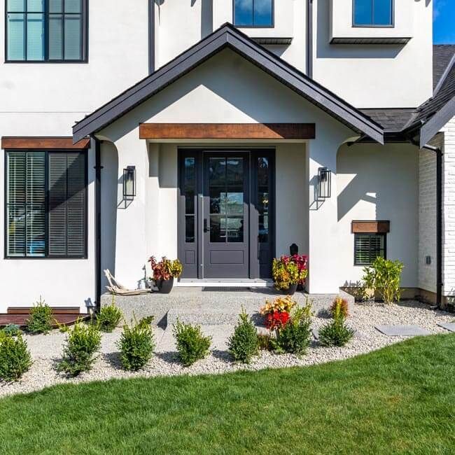 Modern house front entrance with gray door, white exterior, and landscaped garden with flowers and grass