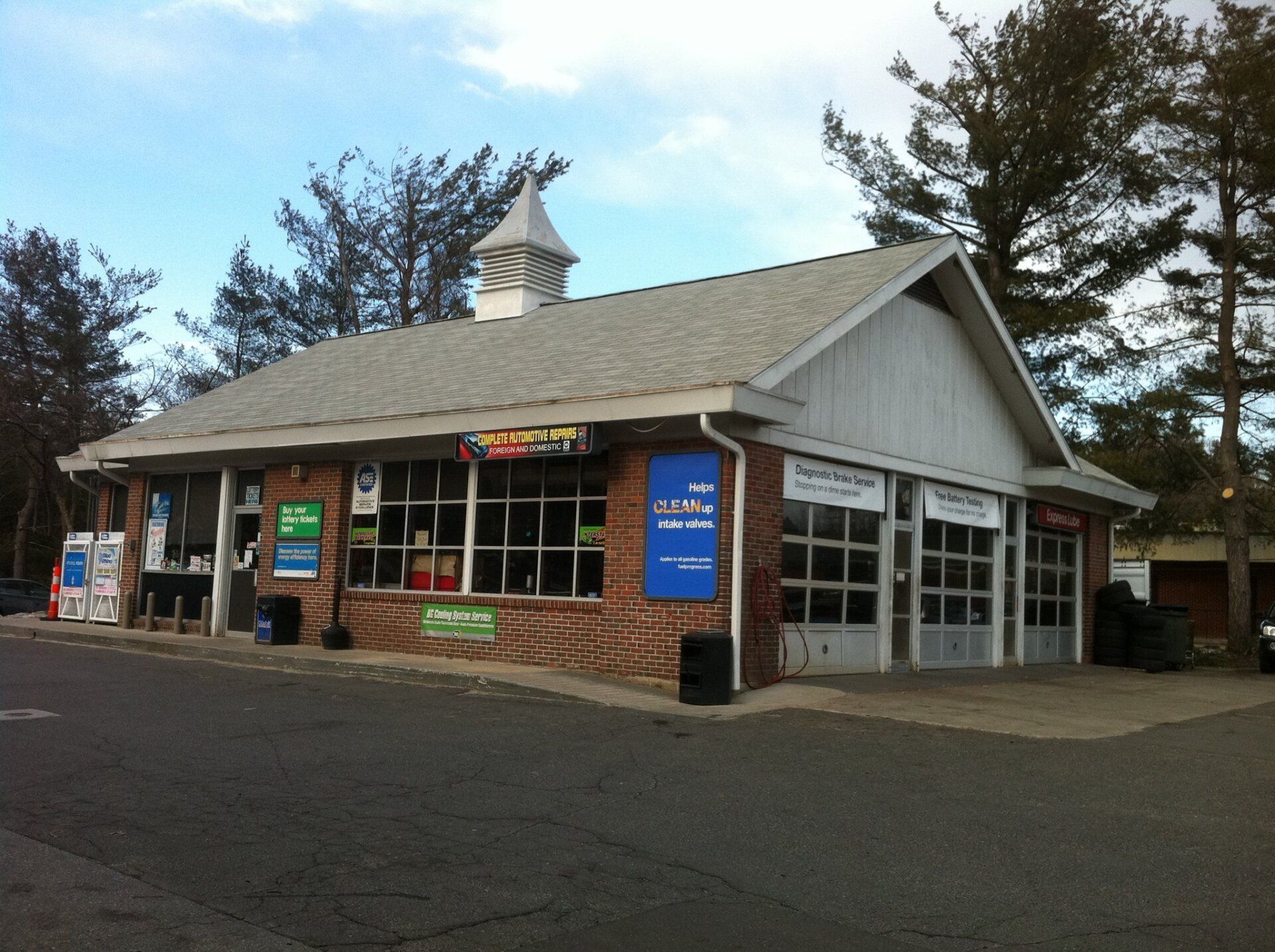 Gas station with brick facade, large windows, and garage bays. Blue signs, white roof, and small steeple.