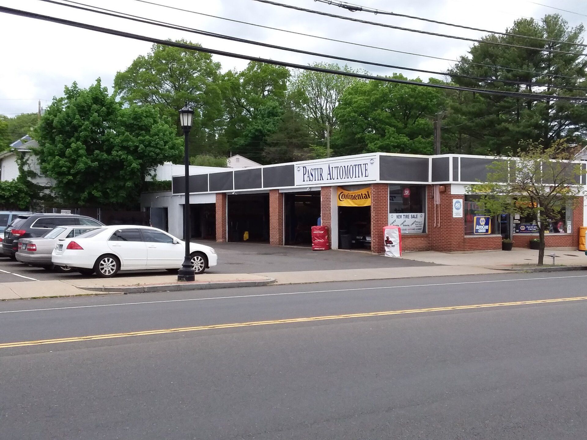 Car repair shop with cars parked in front, trees, and blue sky.