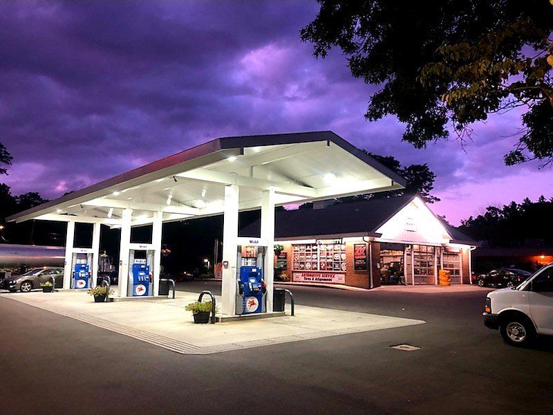 Gas station at dusk with illuminated canopy and convenience store. Purple and pink sky.