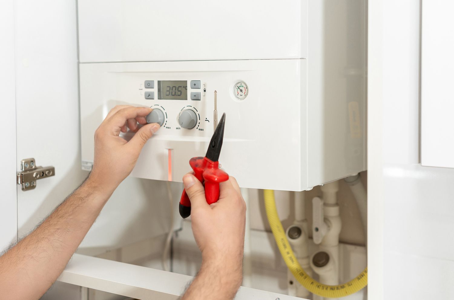 A man is fixing a boiler with a screwdriver.