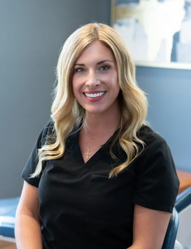 Woman with blonde hair wearing a black scrub top, smiling.