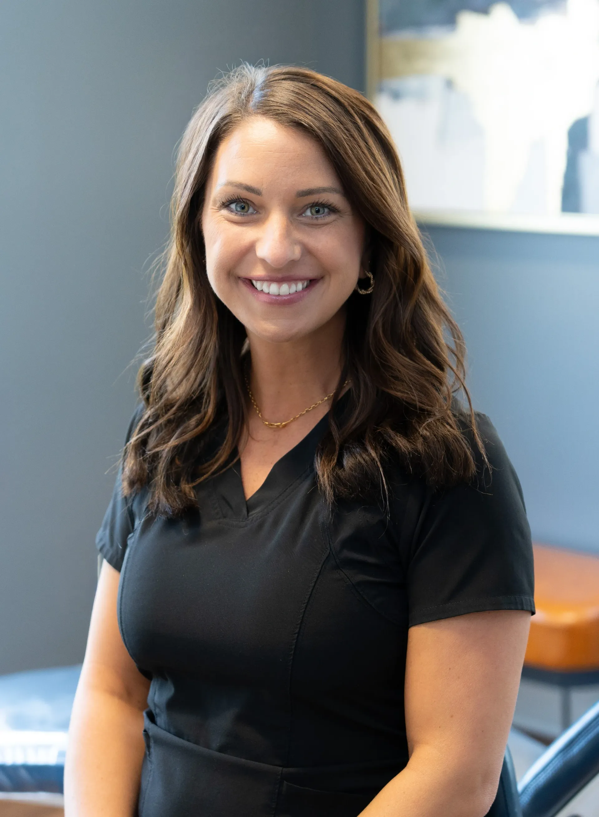 Woman in black scrubs smiles at camera, dark hair, neutral background.