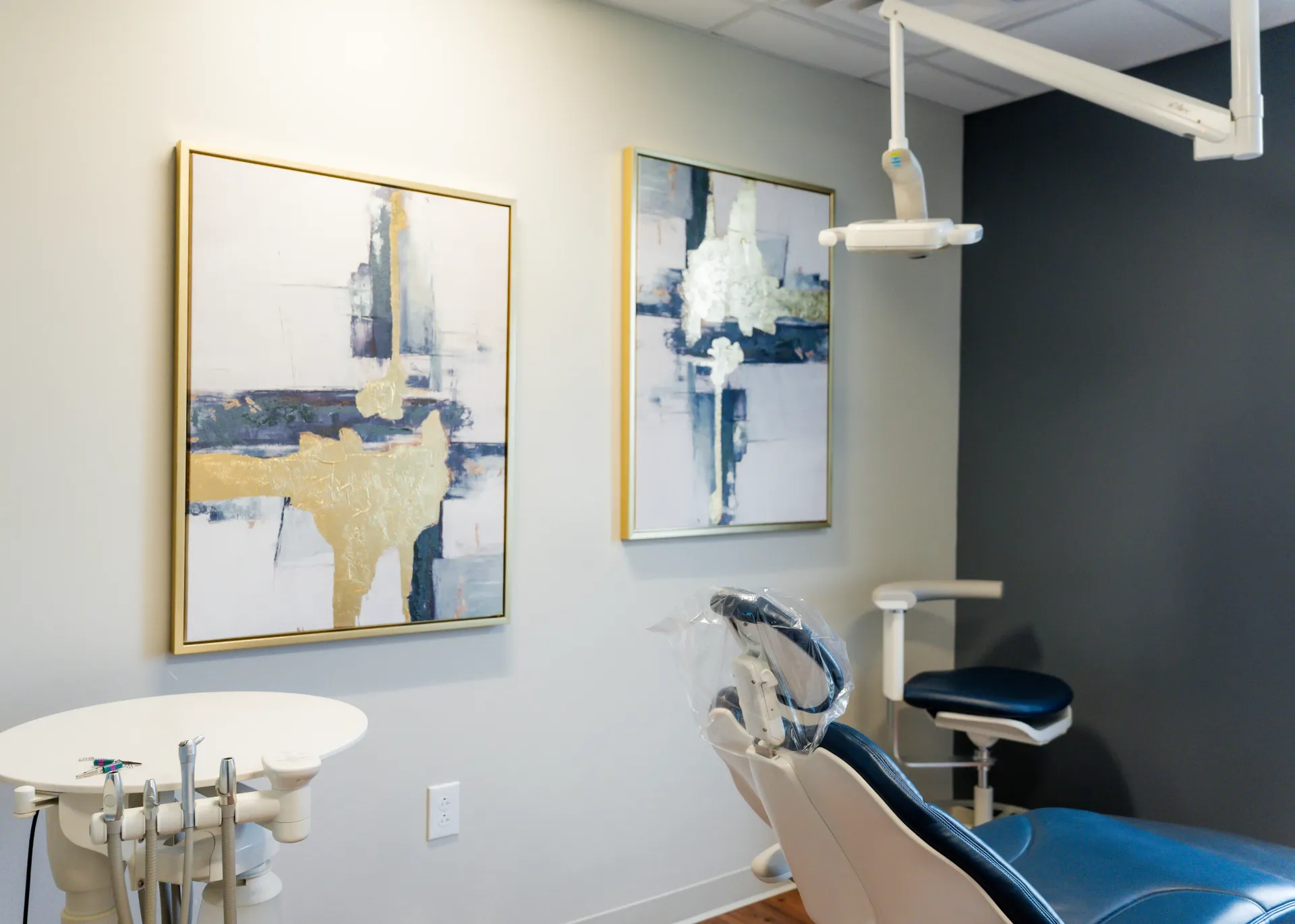 Dental exam room with a chair, art, and equipment. Blue and gold accents.
