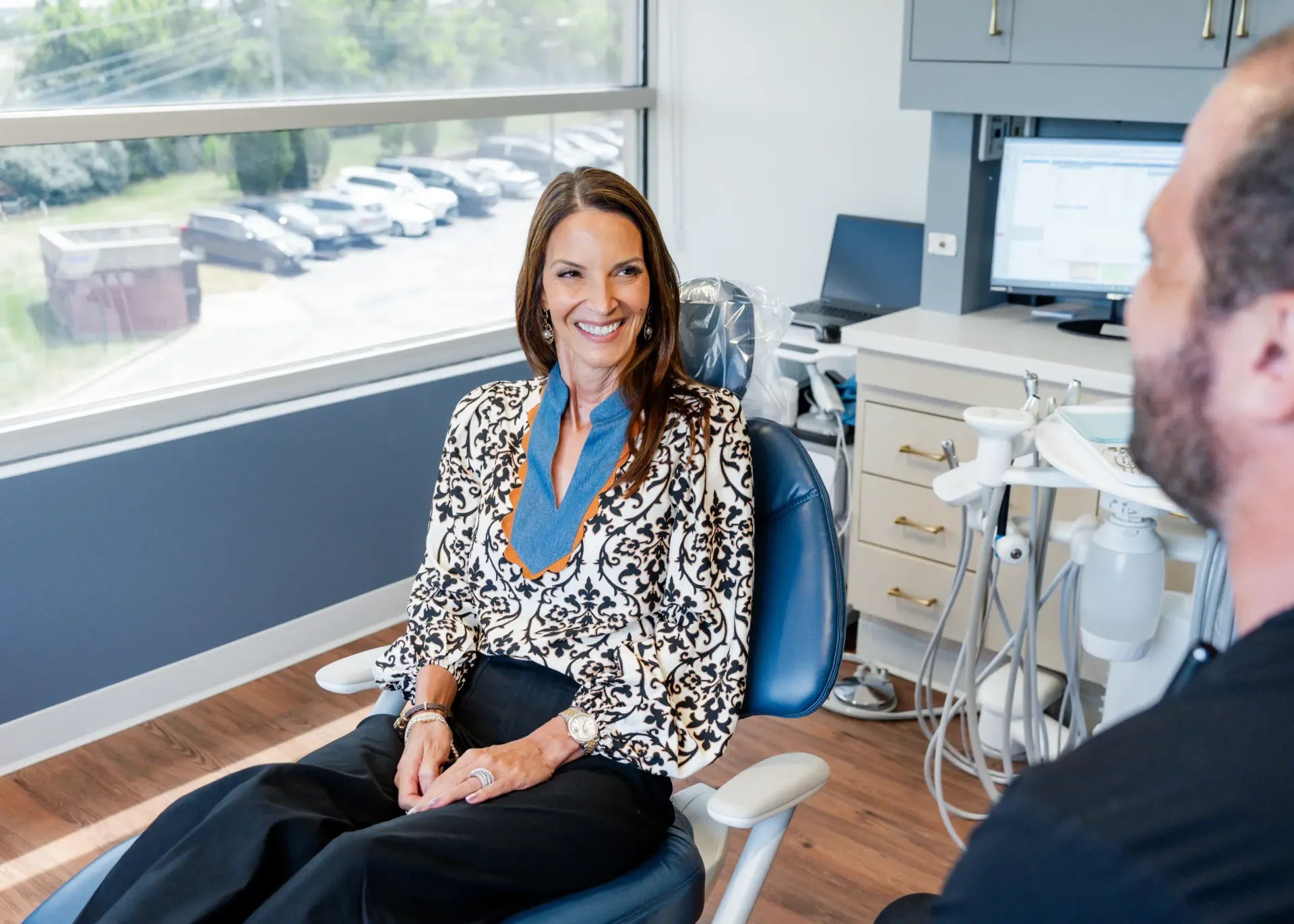 Woman in a dental chair smiling at a dentist in a modern office with a window and equipment.