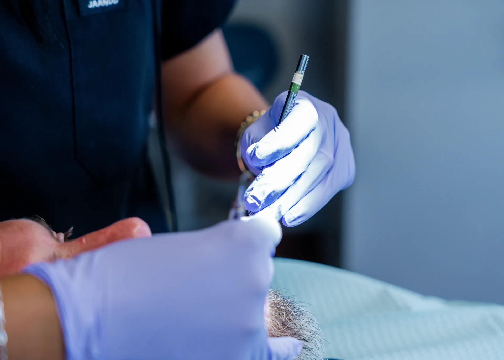 Dentist using a tool on a patient's mouth. Purple gloved hands, bright light.