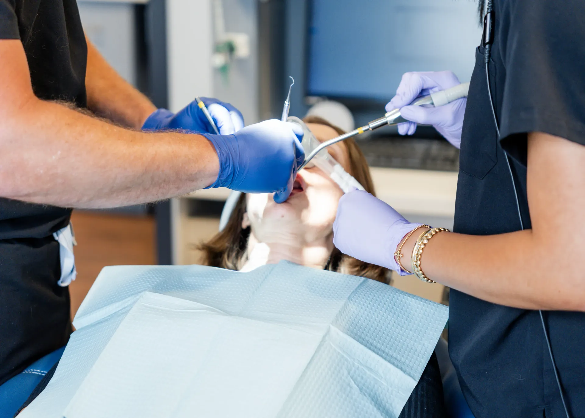 Dentist performing dental work on a patient in a clinic, using tools and wearing gloves.