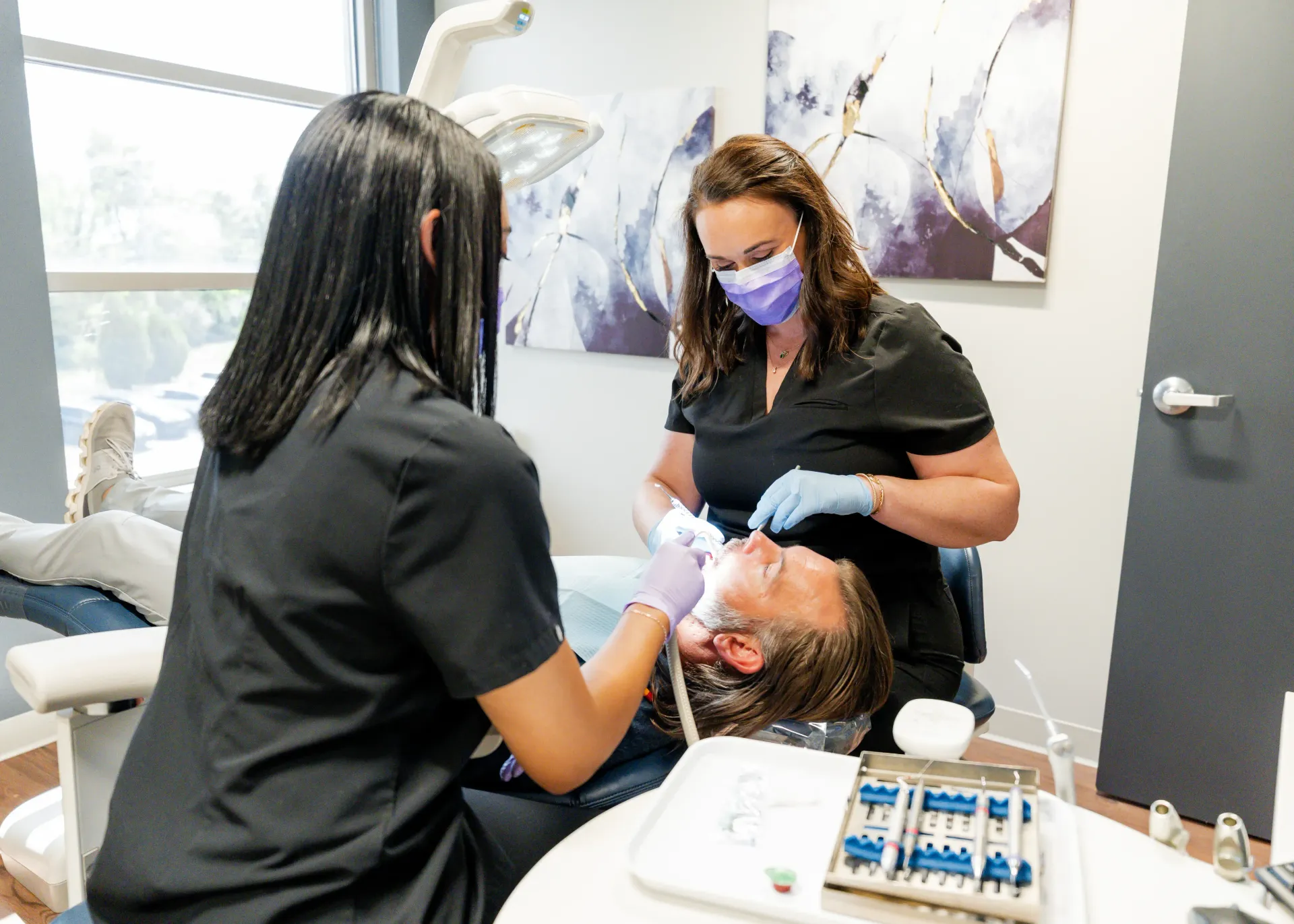 Dentist and assistant working on patient in dental chair, light blue and white room.