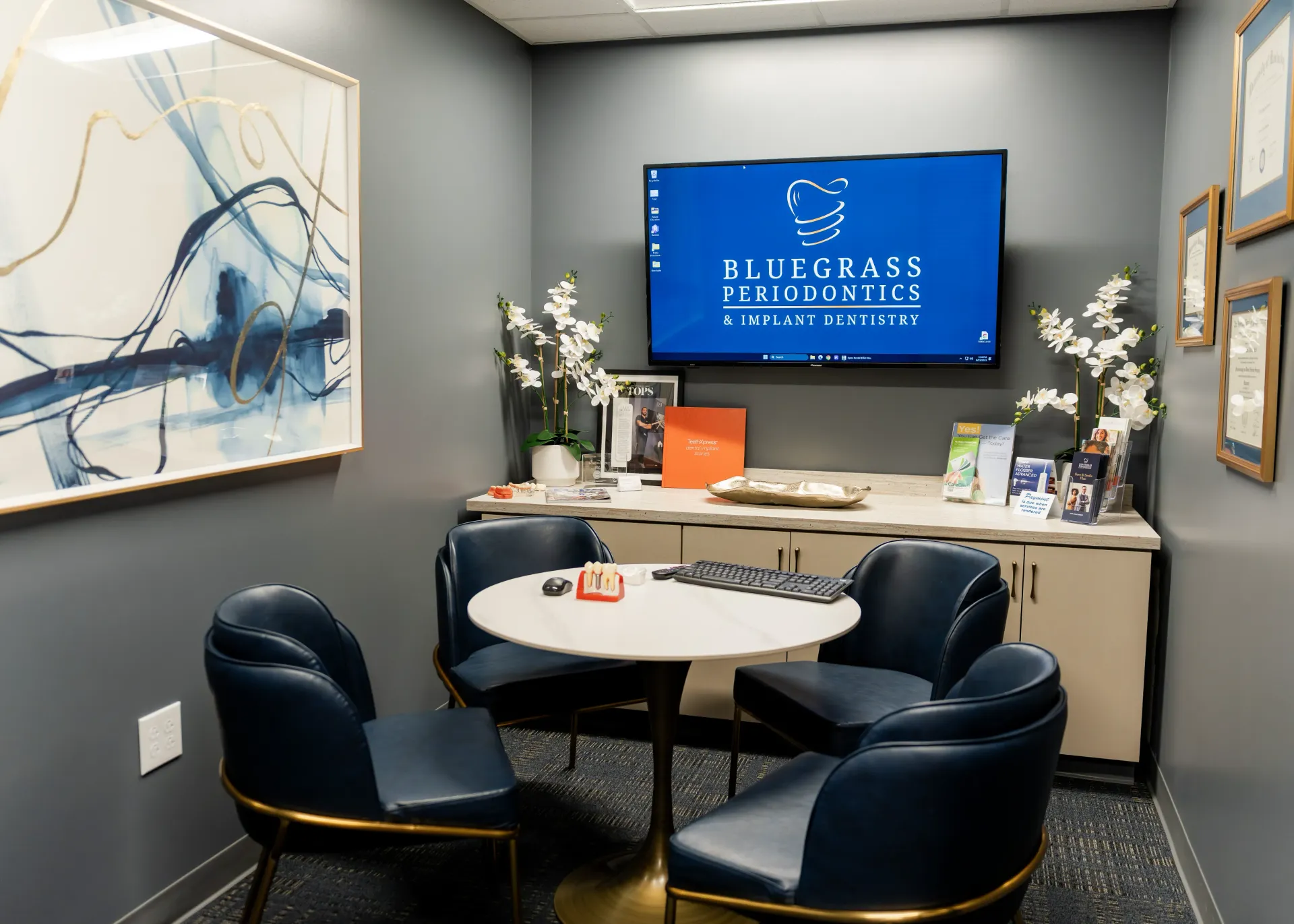 Dental office consultation room with chairs around a small table, TV, and artwork. Blue and white colors.