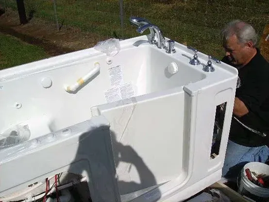 Man installing a white walk-in bathtub outdoors. 