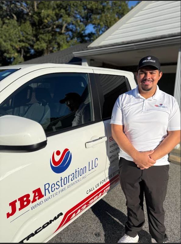 Man stands beside a company truck. The truck has the JBA Restoration logo on it, and the man is wearing a company shirt.
