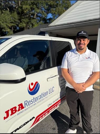 Man stands beside a company truck. The truck has the JBA Restoration logo on it, and the man is wearing a company shirt.