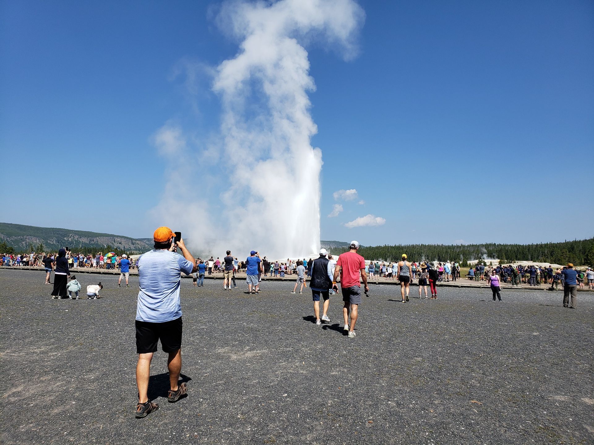 A man is taking a picture of a geyser with a camera.