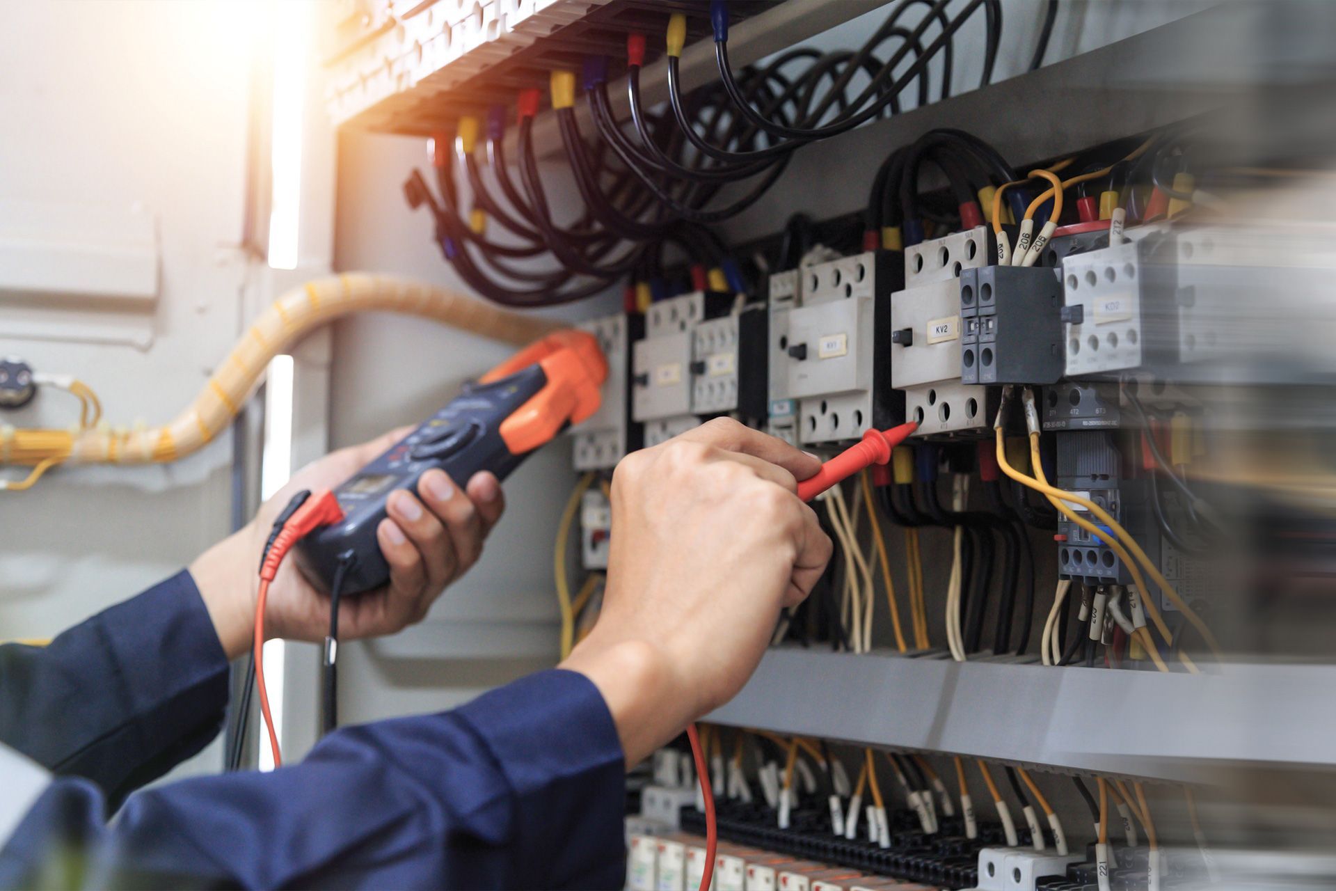 An electrician is working on an electrical panel with a multimeter.