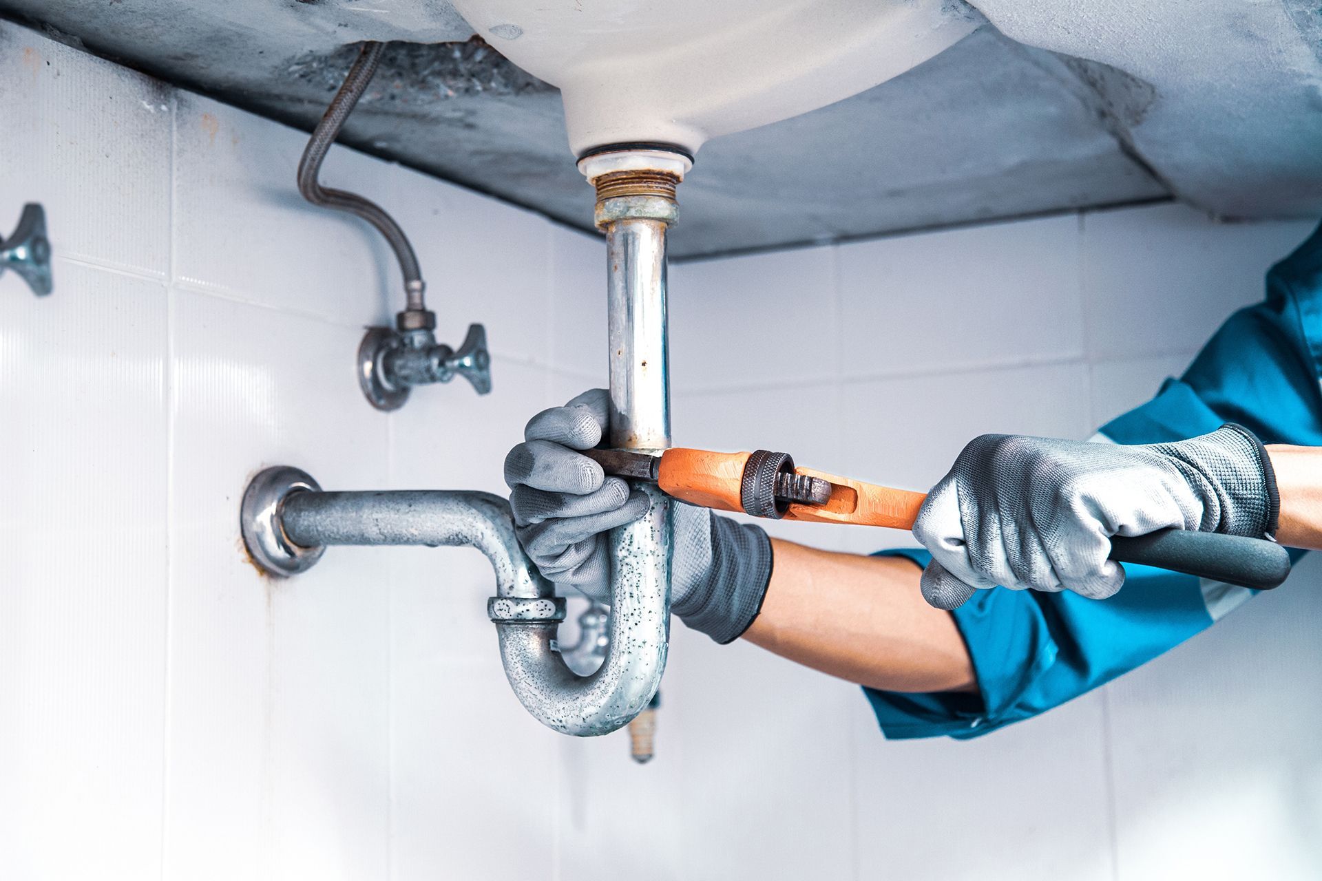 A plumber is fixing a sink pipe with a wrench.