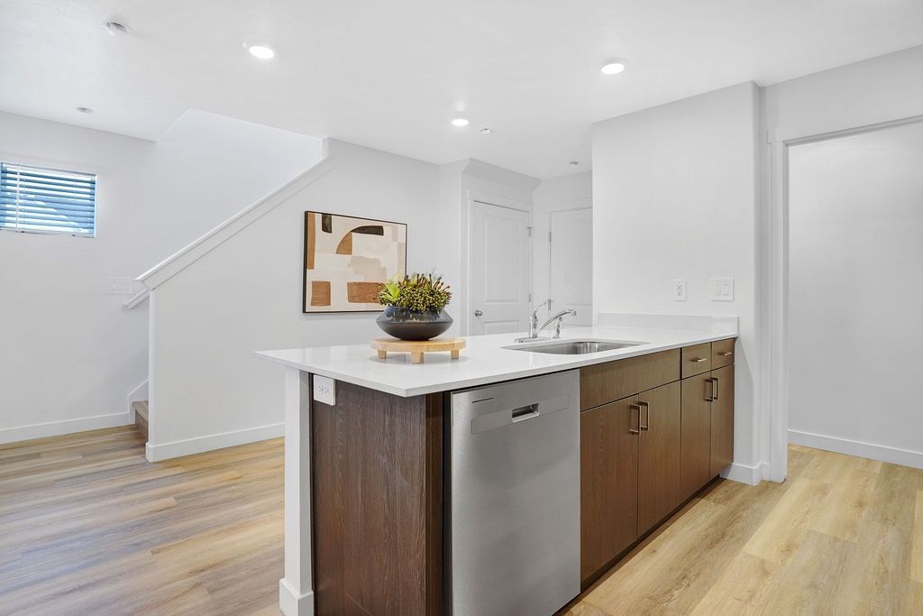 Modern kitchen with island, stainless dishwasher, wood cabinets, and white countertops.
