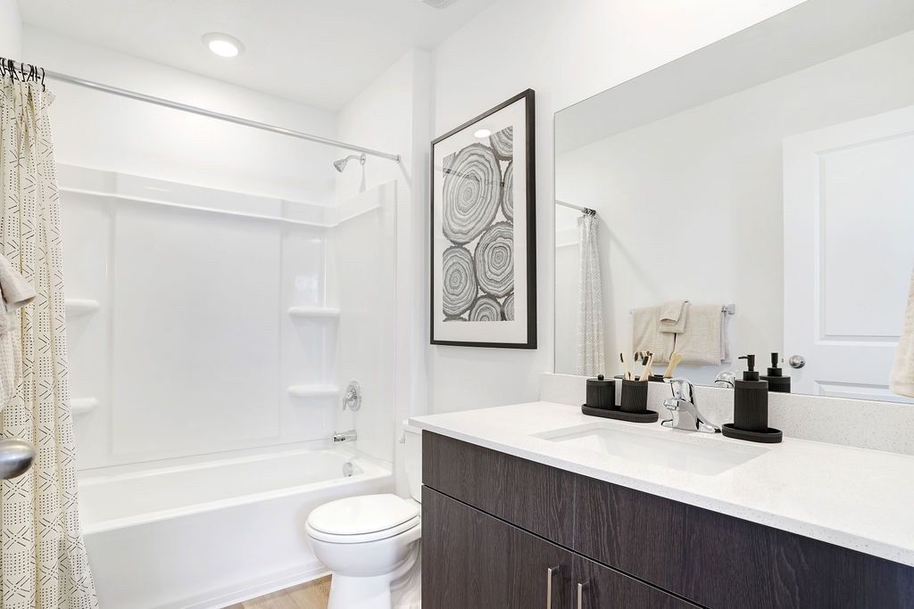 Bright bathroom in a modern apartment: white tub/shower, sink, and dark vanity.