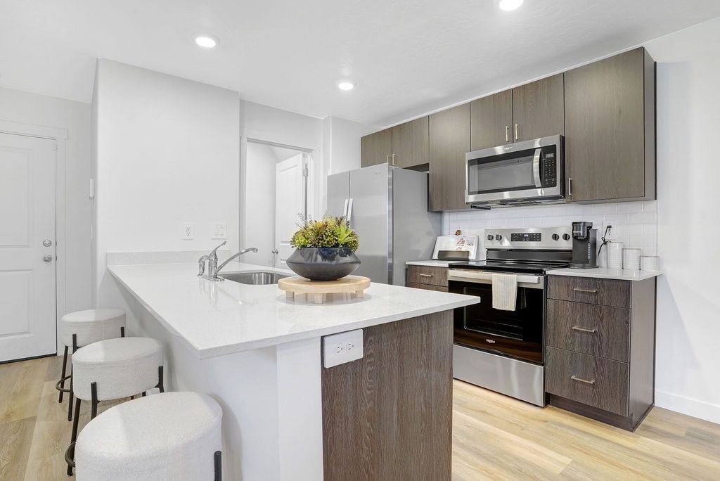 Open-concept apartment kitchen with an island, white countertops, and stainless steel appliances.