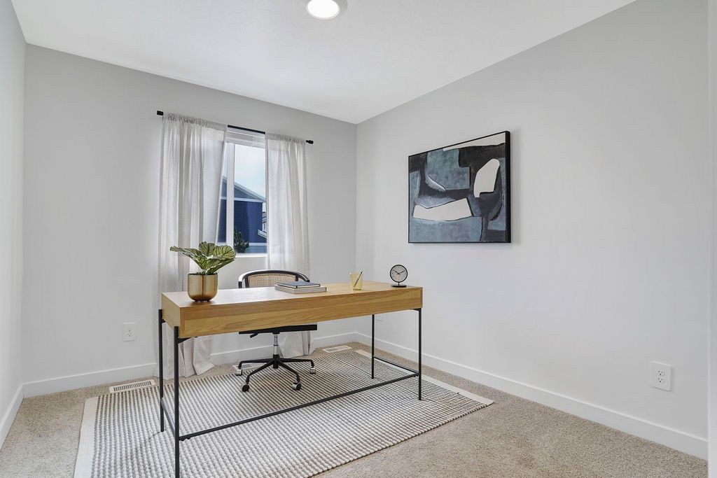 Home office inside an apartment: wooden desk, chair, rug, plant, and abstract wall art.