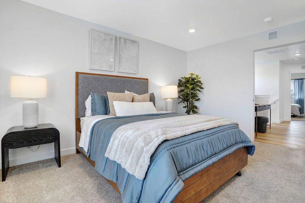 Bedroom with a wooden bed, blue bedding, two nightstands, lamps, and a doorway to a hallway.