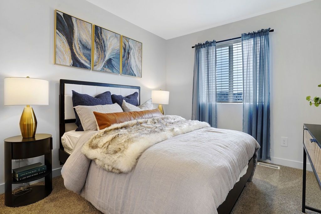 Bedroom in apartment with queen bed, two nightstands, lamps, and blue curtains by the window.