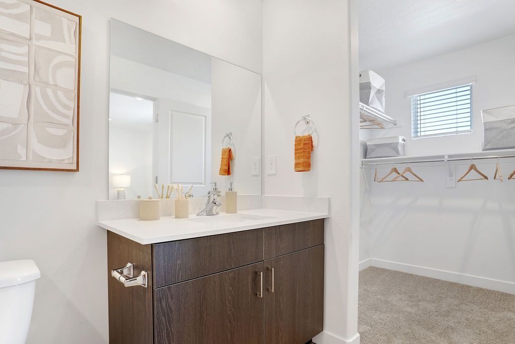 Bathroom vanity with dark wood cabinet, white countertop, large mirror, and an open closet area.