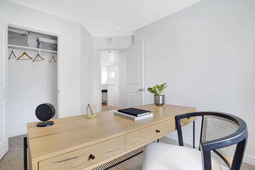 Bright home office area with a wooden desk, chair, and open closet in a modern apartment.