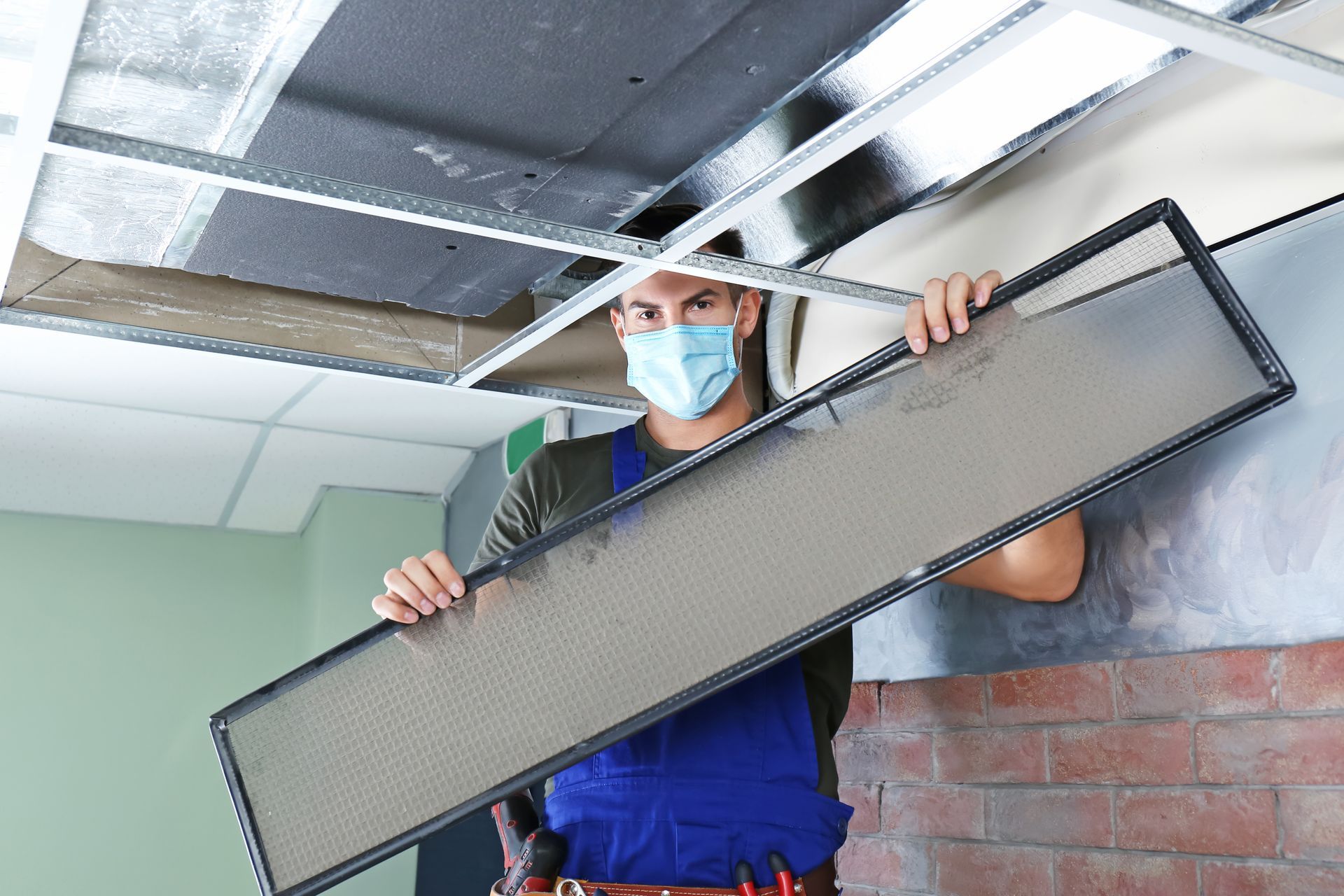 an hvac technitian removes the air filter from a commercial  airvent, the filter is dusty highlighting the question How Often Should Commercial Airvents Be Cleaned and Inspected