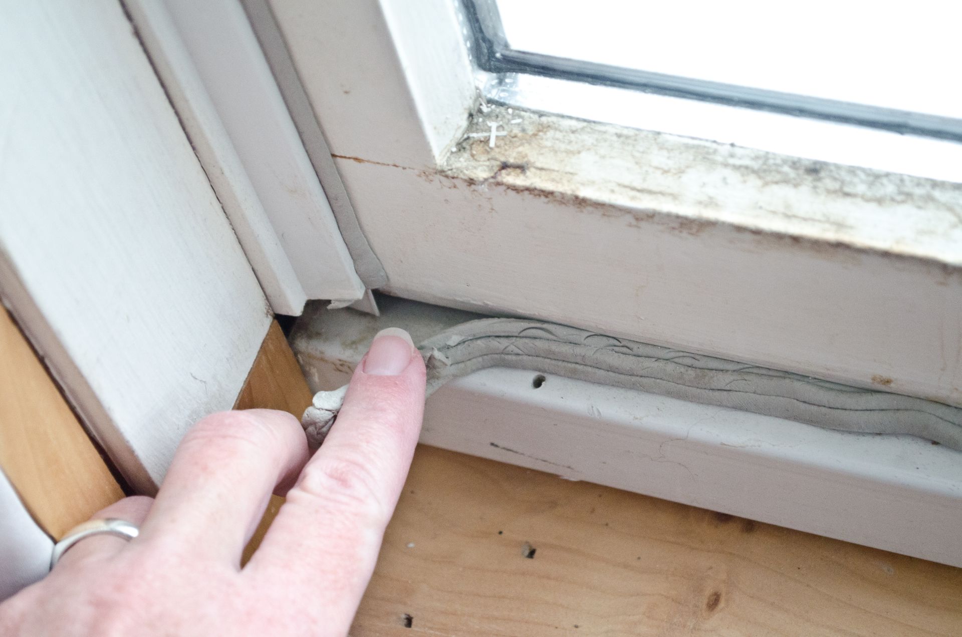 A person is pulling back bad sealing on a historic window, the window needs to be properly preserved