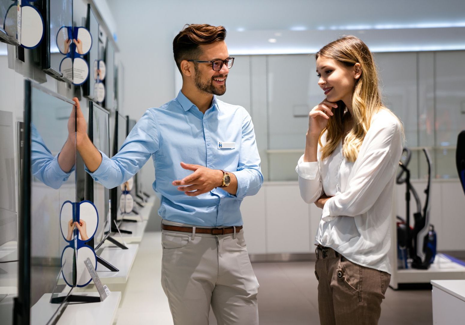 a man wearing a name tag talks to a woman in a store - he's displaying great customer representative skills