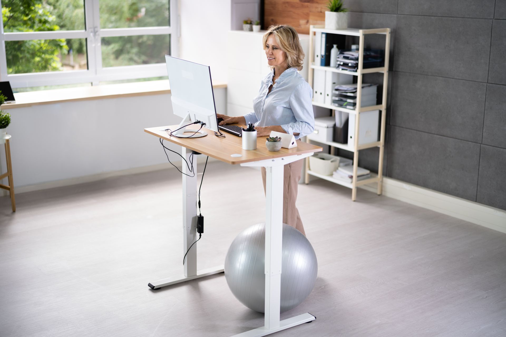 A woman is using a standing desk to provide variety in her work-from-home office allowing her to find pain relief