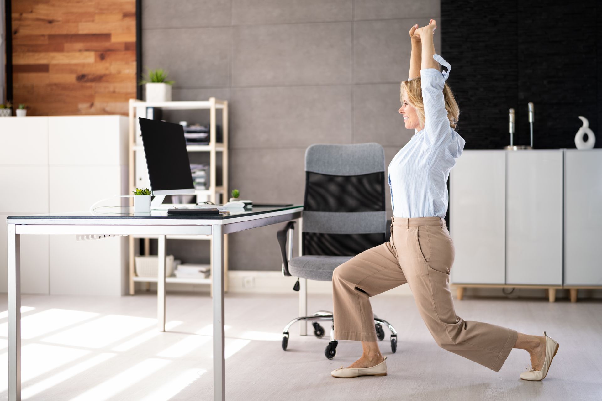 A woman is doing lunges at her desk, remote work pain relief