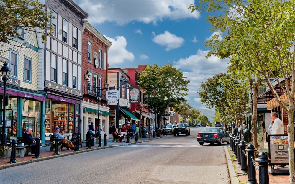 A small town street with a lot of shops and people sitting on benches.