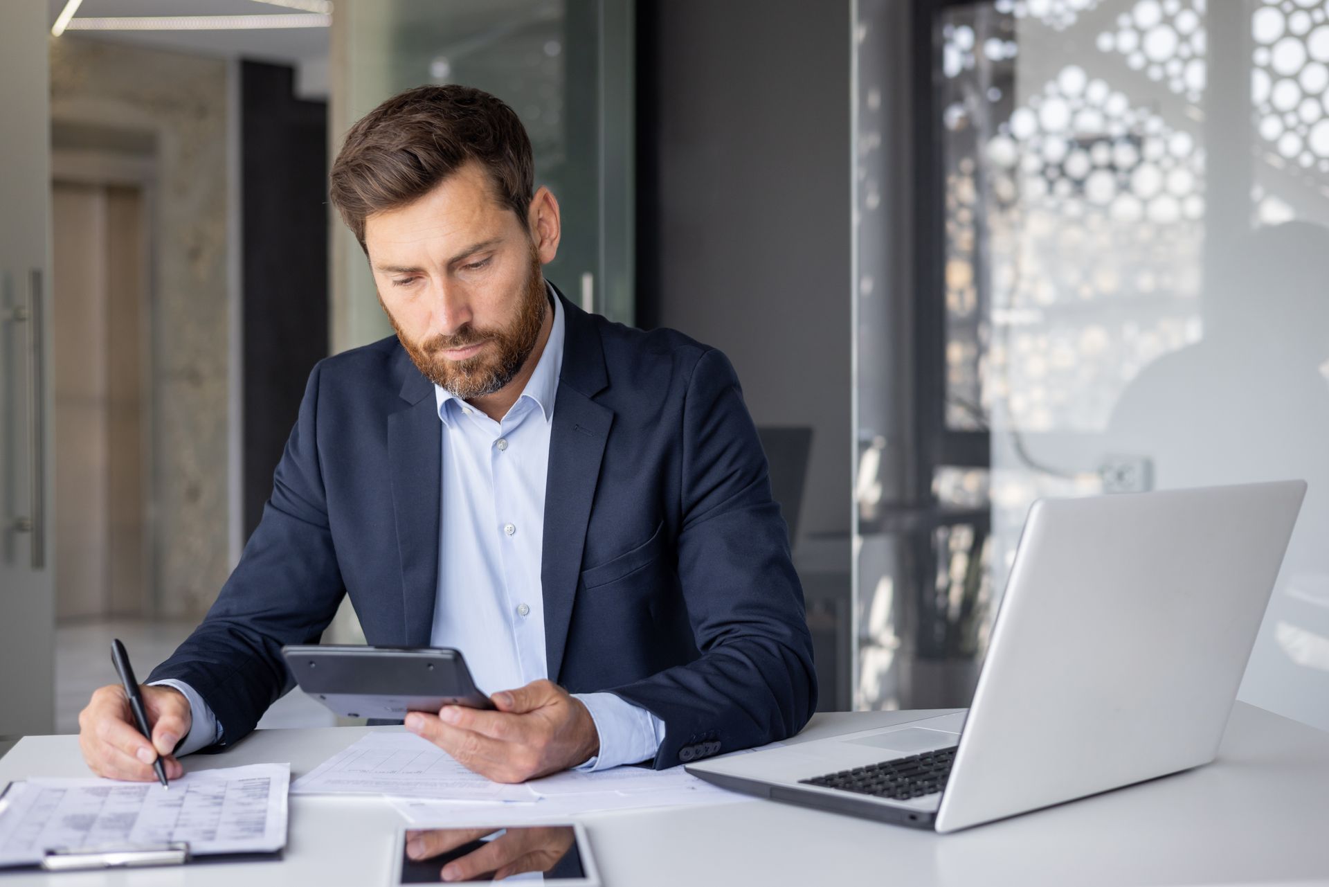 A accountant is sitting at a desk using a tablet and a laptop.