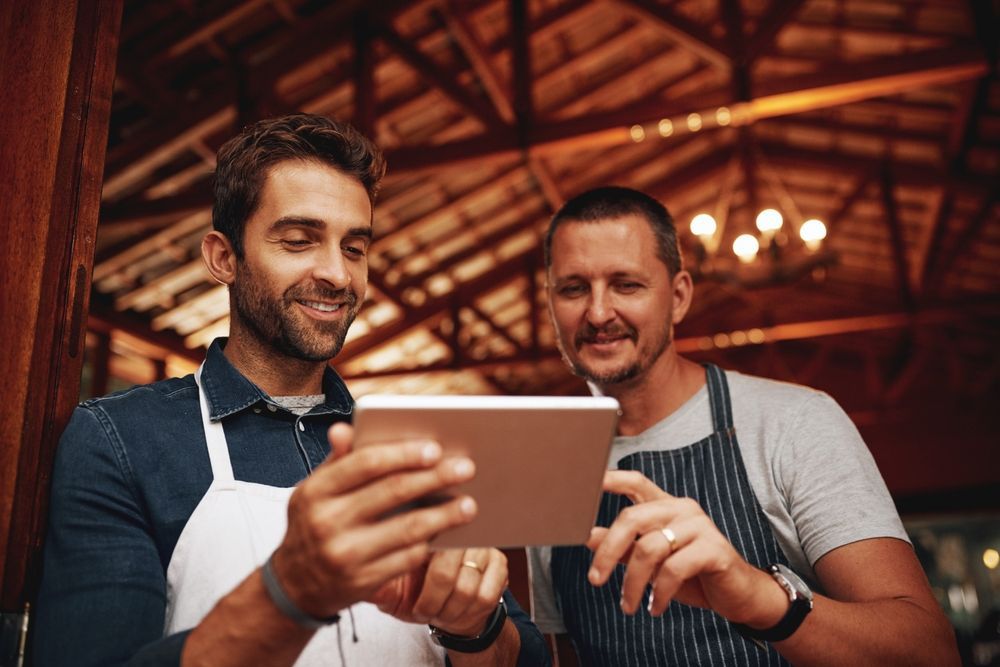 Two men are looking at a tablet together in a restaurant.