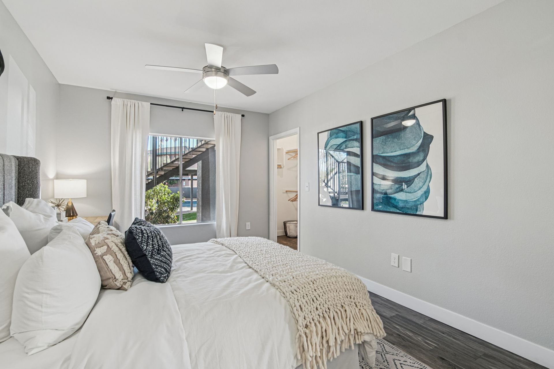 Bedroom with bed, art, window, and ceiling fan. Gray walls, white bedding, and wood-look flooring.