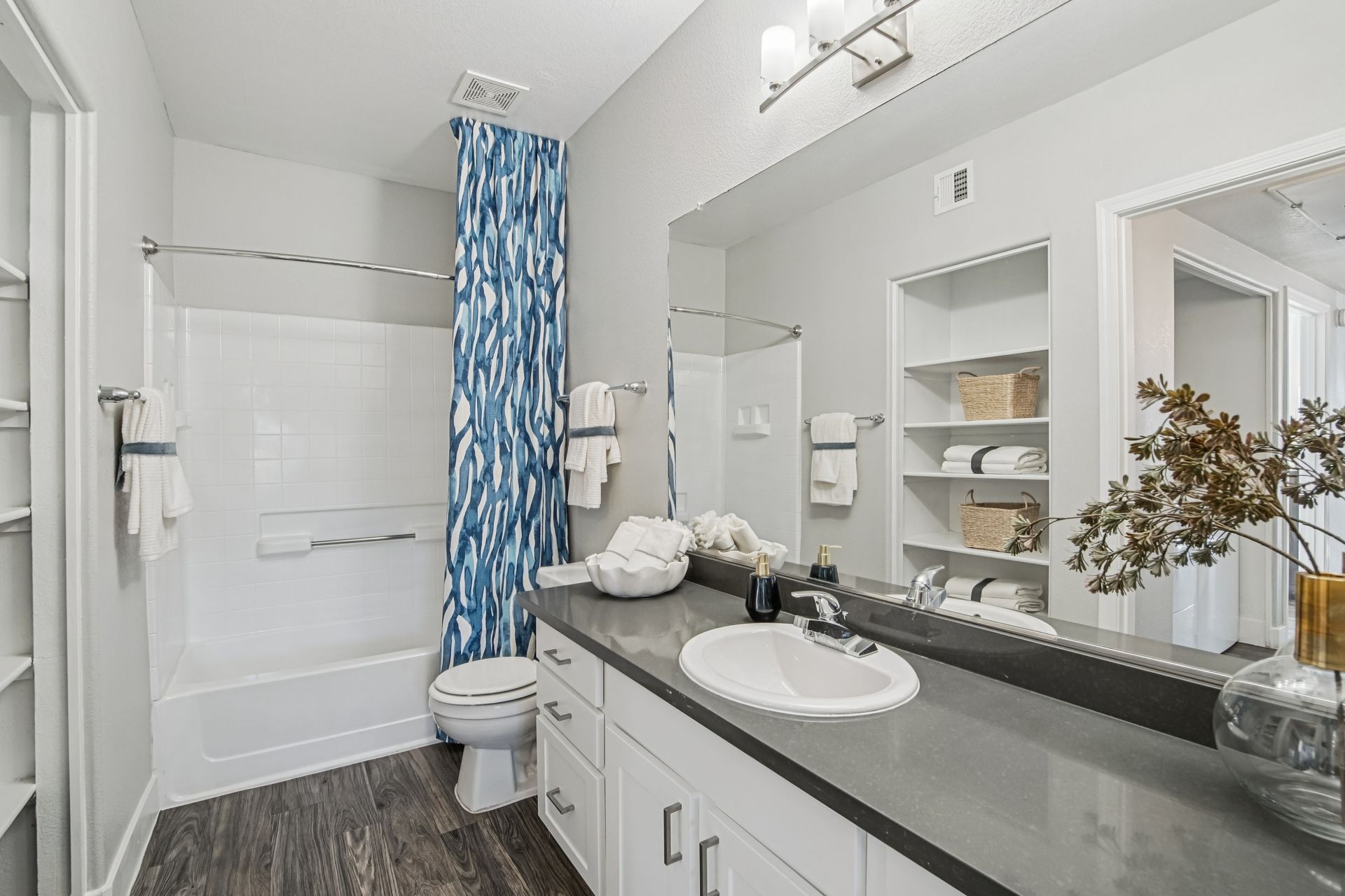 Bathroom with a white tub, toilet, and vanity with a gray countertop. Blue shower curtain and built-in shelves.