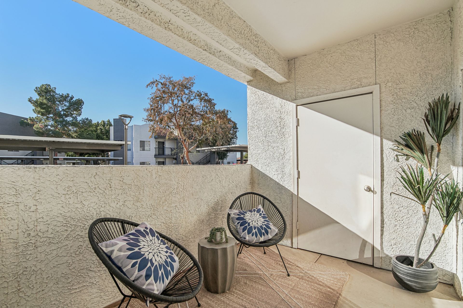 Balcony with chairs, rug, and potted plant, overlooking a view.