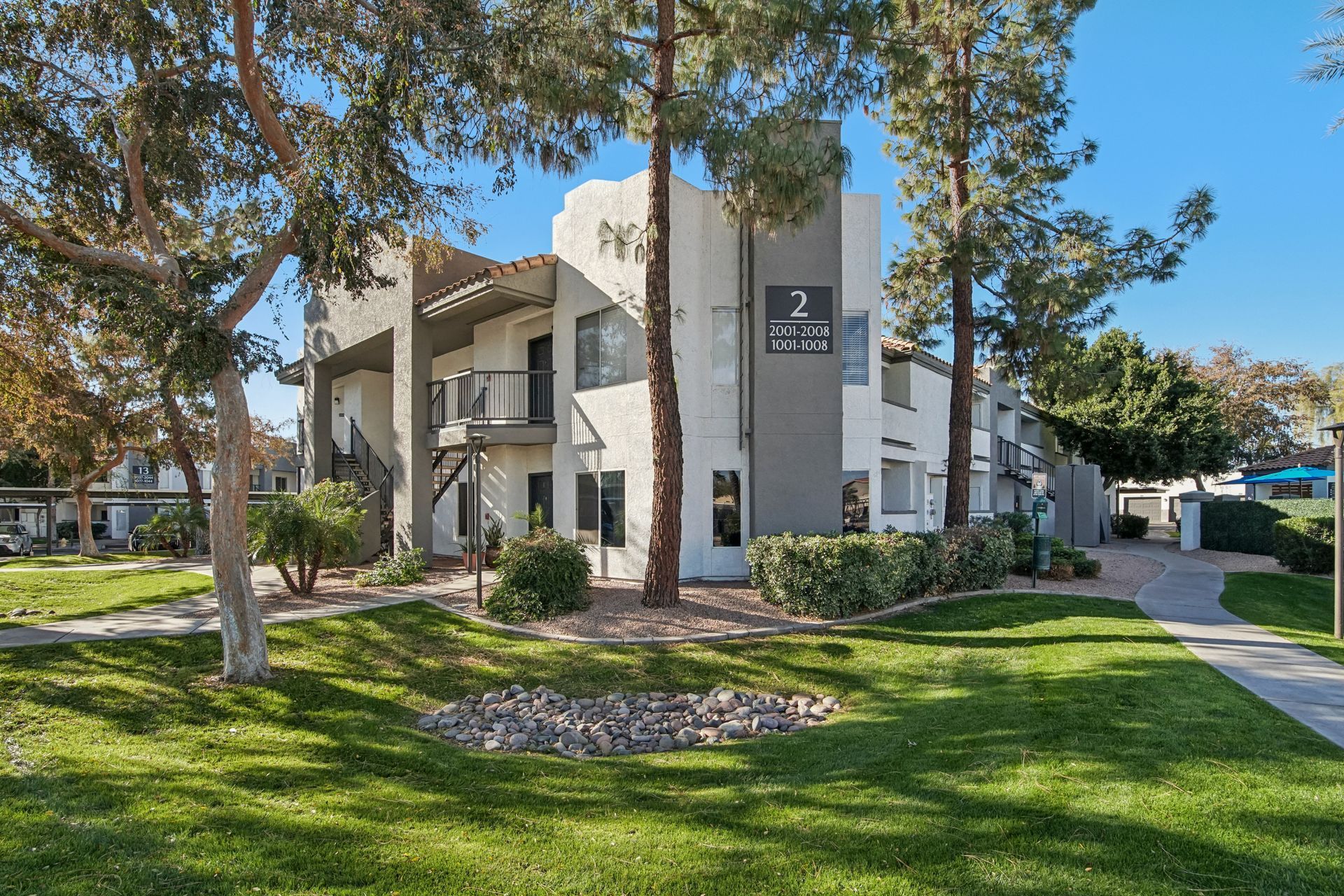 Apartment building exterior with green grass, trees, and blue sky. Building number 