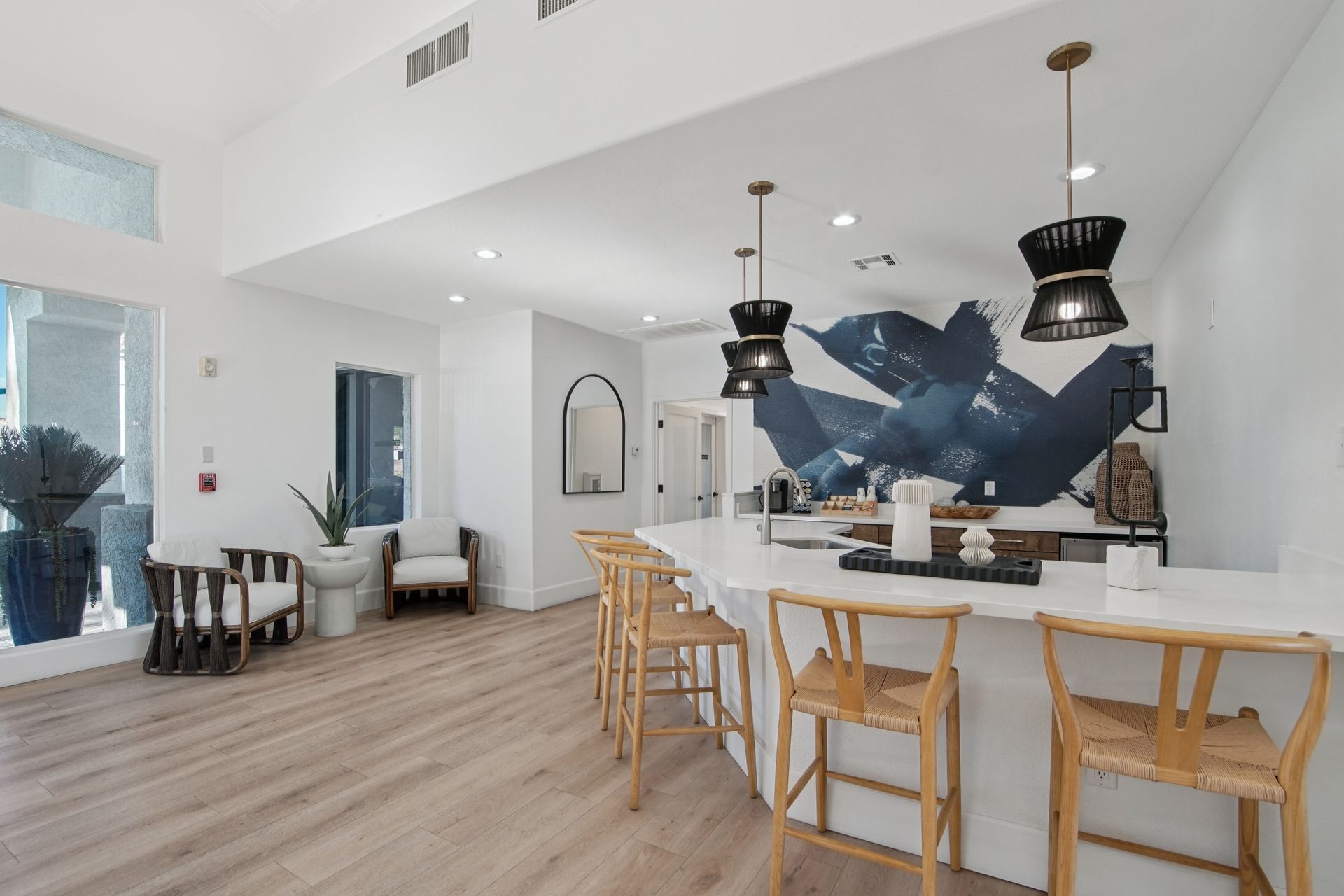 Bright, modern kitchen area with a white countertop and wooden stools. Feature wall with blue art.