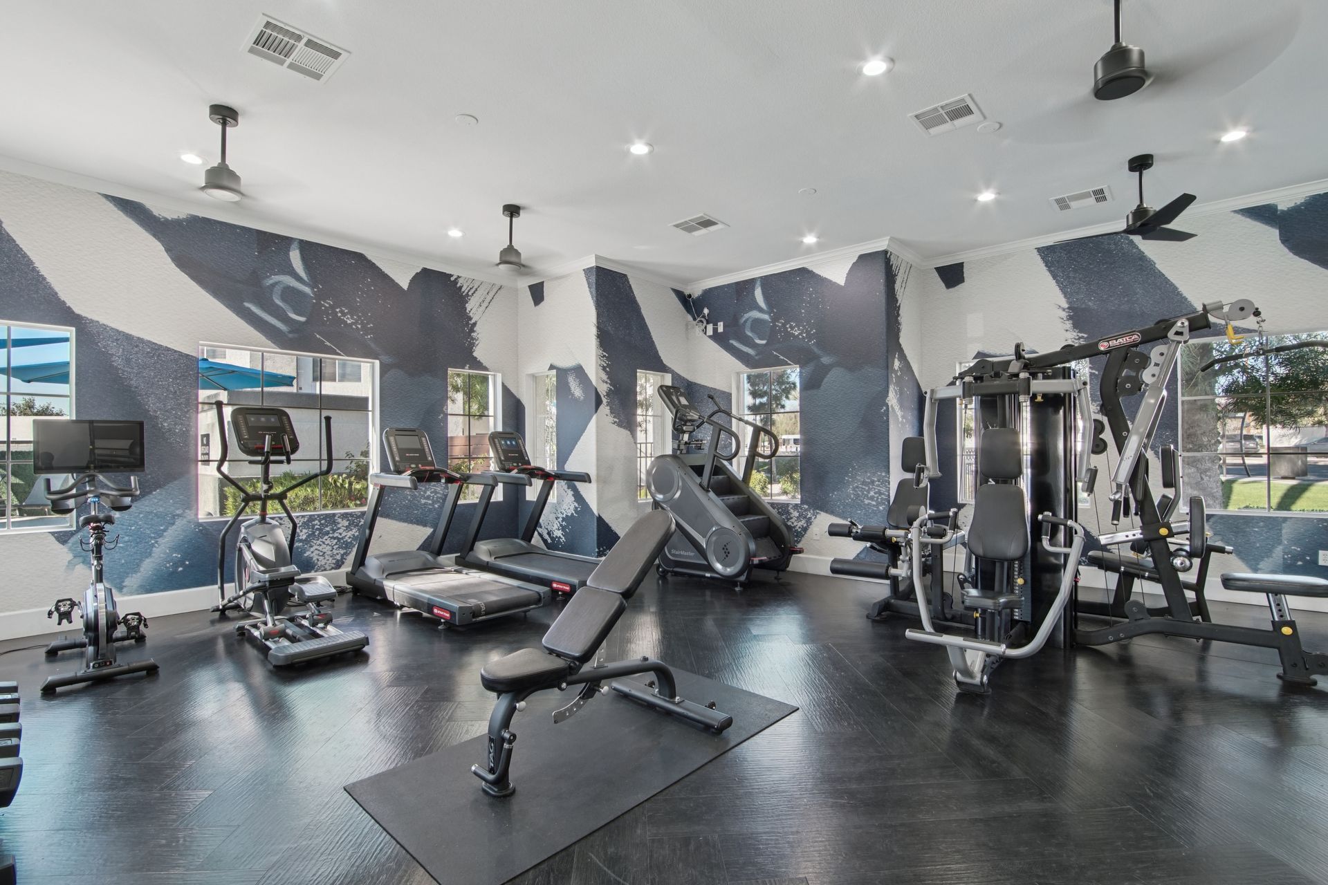 Gym interior with exercise machines, including treadmills, weight benches, and cable machines; blue and white wall design.